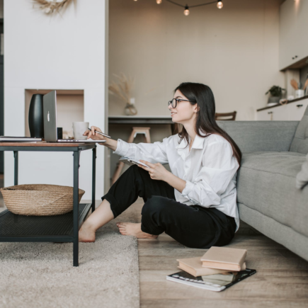 Bespectacled woman with black hear sits on the floor as she learns some valuable skills from home