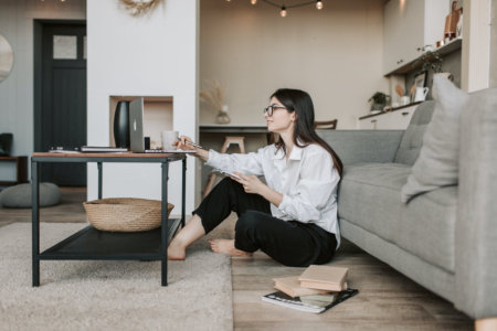 Bespectacled woman with black hear sits on the floor as she learns some valuable skills from home